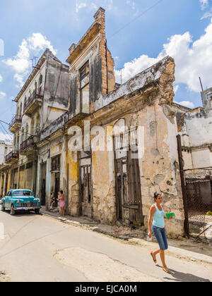 Hispanic Frau geht vorbei an der 1950er Jahre Oldtimer und einer verlassenen, bröckelt, aufbauend auf einer Straße in Havanna, Kuba. Stockfoto