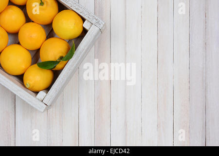 Eine Kiste mit frisch gepflückten Zitronen auf einen rustikalen weißer Holztisch in der oberen linken Ecke des Rahmens. Querformat Stockfoto