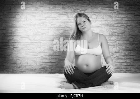 Schöne schwangere Frau auf dem Bett sitzt Stockfoto