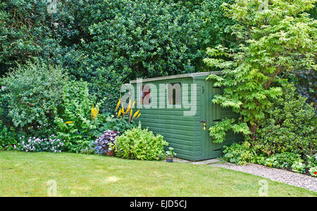 Grüne Gerätehaus in Ecke des englischen Garten mit angrenzenden gemischten Strauch- und Staudenrabatten, Holly Hecke hinter Sommer Stockfoto