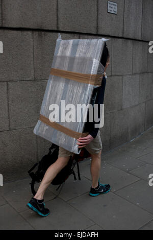 Ein Mann geht durch die City of London mit einer Blase gehüllt Flatscreen-TV auf dem Rücken. Stockfoto