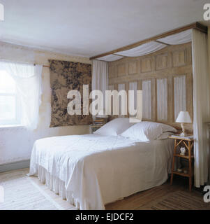 Weiße Vorhänge und Holzvertäfelungen über Bett mit weißen Bettdecke in neunziger Jahre Schlafzimmer mit Gobelin Wandbehang Stockfoto