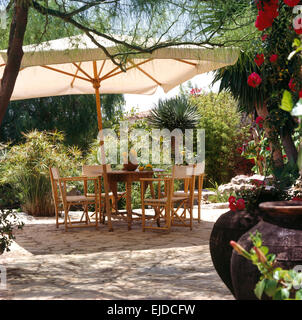 Weißen Schirm über dem Tisch und Regiestühle auf gepflasterten Terrasse im grünen mallorquinischen Garten Stockfoto