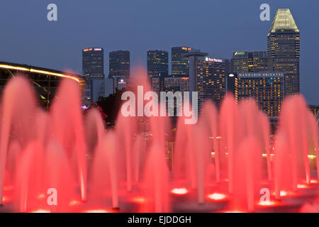 Rote Fontänen außerhalb des Fullerton Bay Hotel mit der Singapur Night Skyline im Hintergrund. Stockfoto