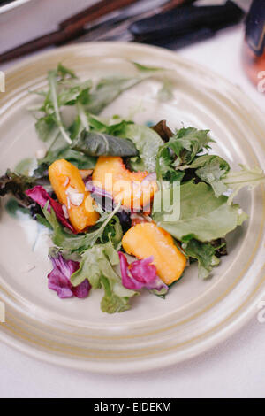 Ein Teller mit frischen Salatblättern und Scheiben von frischem Pfirsich Obst. Stockfoto