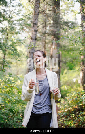 Eine Frau steht auf einer Lichtung im Wald hält zwei große Gläser Champagner. Stockfoto