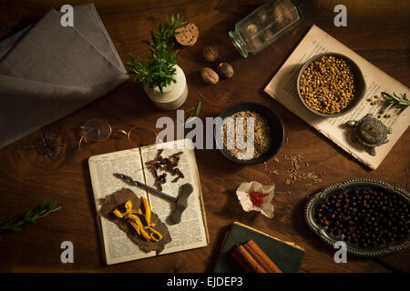 Tisch mit einer Vielzahl von Gewürzen und Aromaten, Koriander, Muskatnuss, Safran, Nelken und Rosmarin und zwei alten Rezeptbüchern. Stockfoto