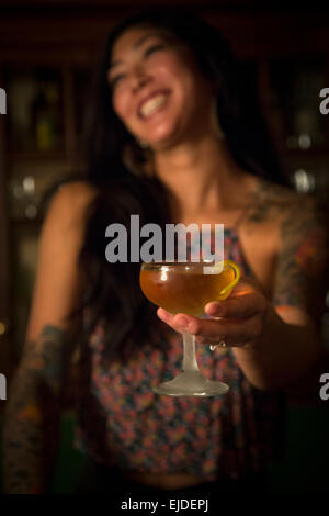 Eine Frau hält ein Cocktailglas in einer Bar. Stockfoto