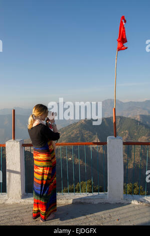 Eine weibliche Touristen in einem bunten Kleid Fotografieren von Kunjapuri Tempel in der Nähe von Rishikesh, Indien, mit Blick auf den Himalaya bei Sonnenuntergang Stockfoto