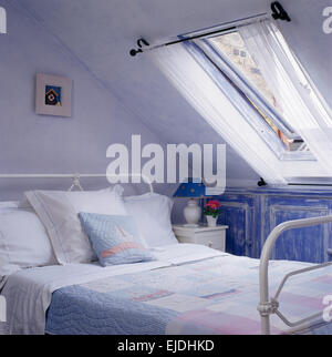 Velux-Fenster über weißen Schmiedeeisen Bett Flickenteppich mit weißen Leinen Kissen in Mansarde Stockfoto