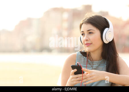 Ehrliche Mädchen aufmerksam und hören die Musik mit einem smart-Phone und wegsehen Stockfoto