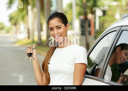 Junge Erwachsene hispanic Frau Tasten des weißen Neuwagen, stützte sich auf automatische Tür. Sie lächelt und schaut stolz in die Kamera, zeigt th Stockfoto