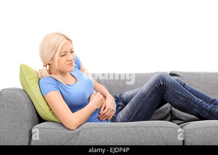 Blonde Frau Gefühl Magenschmerzen sitzt auf einem grauen Sofa isoliert auf weißem Hintergrund Stockfoto