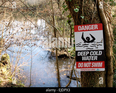 Gefahr tiefen kalten Wasser schwimmen nicht Schild an einem Baum oberhalb einer überfluteten Steinbruch Grube, des Bischofs Tawton, Devon, UK genagelt Stockfoto