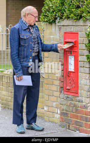 Älterer Mann Entsendung einen Brief in einer Royal Mail Wand montiert Briefkasten in England, UK. Stockfoto