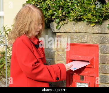 Applying Frau Entsendung einen Brief in einen Royal Mail Wand montierten Briefkasten, in England, UK. Stockfoto