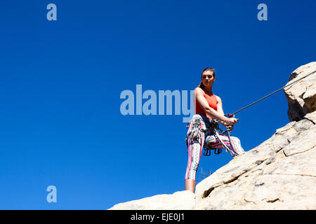 Eine Frau trägt ein rotes Tank Top und gestreifter Hose belays beim Klettern am unteren Felsen von Gibraltar in Santa Barbara, Kalifornien. Stockfoto