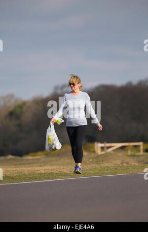 Eine ältere Frau ist Joggen im New Forest National Park ein paar Morrisons Tragetaschen Wurf abholen. Stockfoto