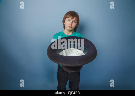 Europäisch anmutende junge von zehn Jahren Bettler Holding Hut in der Hand auf blauem Hintergrund Stockfoto