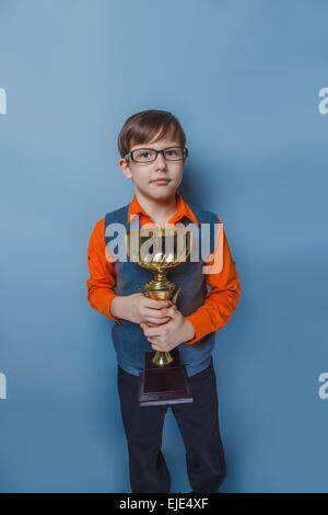 Europäisch anmutende junge von zehn Jahren in Gläsern hält eine Tasse Award Freude auf blauem Hintergrund Stockfoto