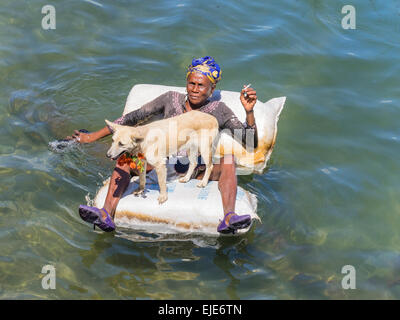 Ein Afro-kubanischen Bettlerin liegend auf einem Floß im Meer von Cayo Granma. Sie ist von ihrem weißen Hund begleitet. Stockfoto