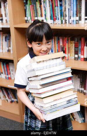 Grundschule Mädchen hält eine große Anzahl von Büchern im Lesesaal Stockfoto