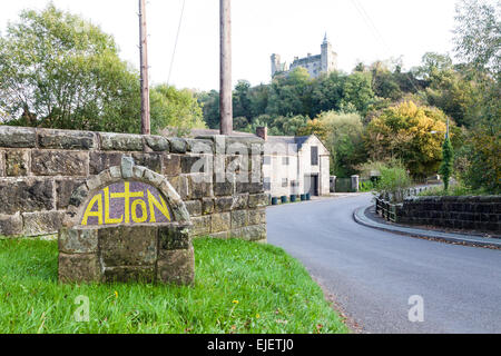 Ein Ortsschild von Alton Staffordshire, die Heimat von Alton Towers mit Alton Burg im Hintergrund Stockfoto