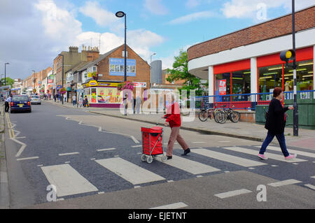 Ältere Frau schieben Einkaufswagen über Zebrastreifen in Aylesbury, Buckinghamshire, England Stockfoto