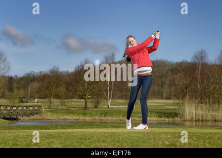 Frau Golfer schlagen einen Golfball mit ihrem Fahrer stehen in der Follow through Position nach dem Schlaganfall Stockfoto