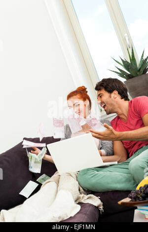 Nahaufnahme sehr glückliches junges Paar mit Laptop sitzen auf der Couch und Euro-Geld in die Luft werfen. Stockfoto