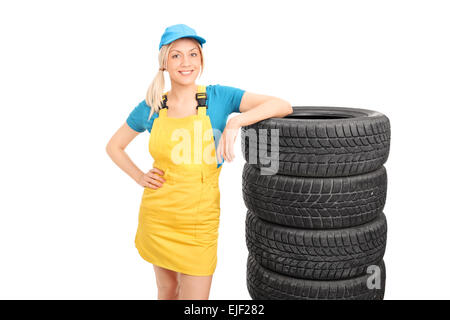 Schöne weibliche Mechaniker in einem gelben Uniform und eine blaue Kappe stand neben einem Stapel Reifen isoliert auf weißem Hintergrund Stockfoto