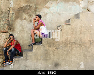 Afro-kubanische zu zweit, ein Männchen und ein Weibchen, beide in ihren 20ern, draußen auf eine Betontreppe an der Seite eines Hauses. Stockfoto