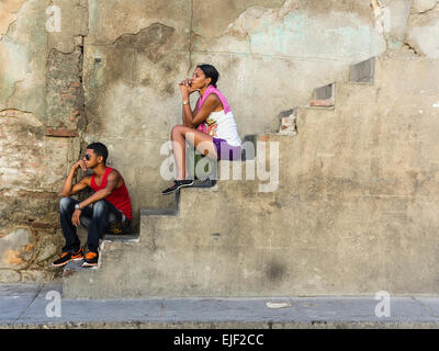 Afro-kubanische zu zweit, ein Männchen und ein Weibchen, beide in ihren 20ern, draußen auf eine Betontreppe an der Seite eines Hauses. Stockfoto