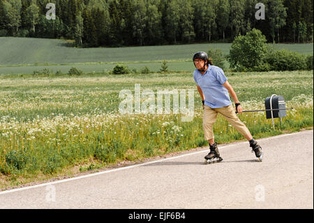 Senior woman kräftig trainieren. Er ist Nordic Inline-skating auf einer Landstraße durch die Felder. Es gibt ein Briefkasten an der Seite des Stockfoto