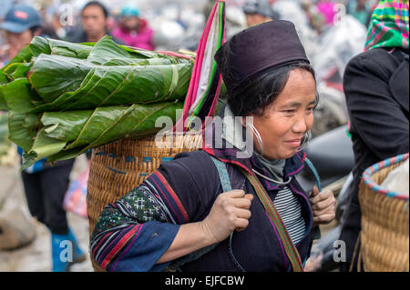 Hmong Frau trägt einen Korb mit grünen Blättern auf einem Markt in Sapa, Vietnam Stockfoto