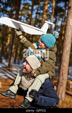 Sohn sitzt auf Vater um den Hals und hält Spielzeug Flugzeug Stockfoto