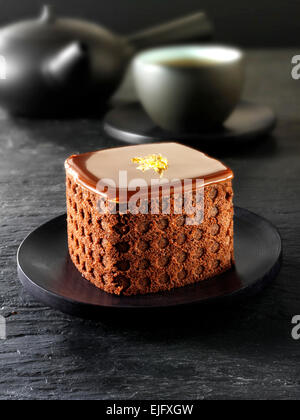 Eine handgemachte Patisserie Spezialität reichen verwöhnenden Schokoladenkuchen mit Tee in einem schwarzen Setting Stockfoto
