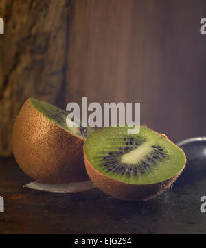 Eine Kiwi schneiden in der Mitte mit einem silbernen Messer auf einem rustikalen Hintergrund Stockfoto