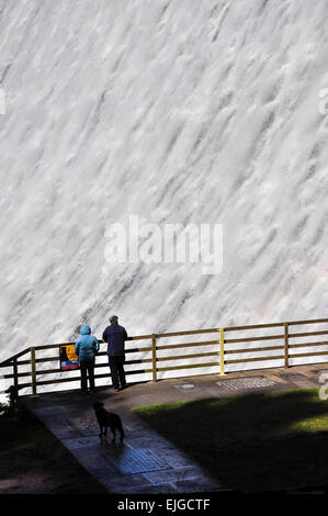 Zwei Personen und ihr Hund stehen, Blick auf das Wasser kaskadenförmig Derwent Damm im Peak District, Derbyshire. Stockfoto