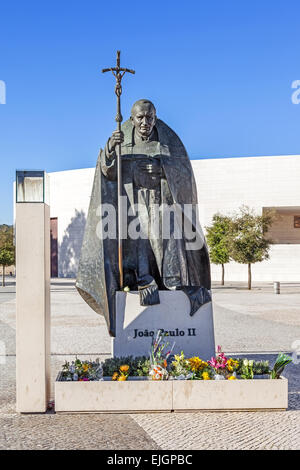 Heiligtum von Fatima, Portugal. Statue von Papst Johannes Paul II. mit der Basilika der Heiligen Dreifaltigkeit im Hintergrund Stockfoto