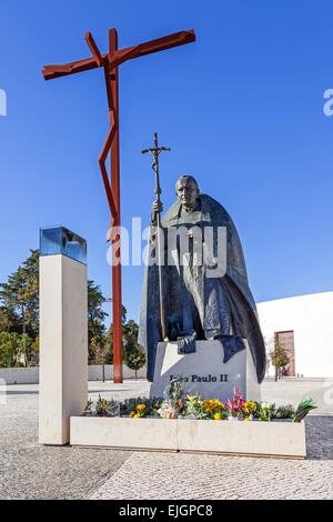 Heiligtum von Fatima, Portugal. Statue von Papst Johannes Paul II. mit dem High-Kreuz und die Basilika der Heiligsten Dreifaltigkeit im Hintergrund Stockfoto