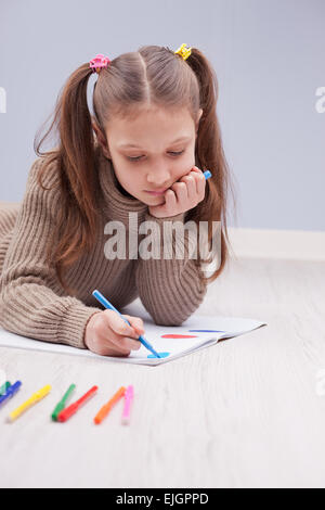 kleines Mädchen auf dem Boden auf ihrem Notebook mit Filzstiften ausmalen Stockfoto