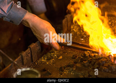 Ein Schmied schmiedet roten heißen Stahl über der Flamme in einem Metall-Shop in Charleston, SC Stockfoto