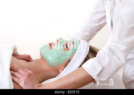 Schöne Frau genießt eine Schultermassage von einer Masseurin, gelegt und mit geschlossenen Augen während einer grünen Schlamm Thalasso Gesichtsbehandlung beaut Stockfoto
