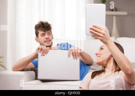 junge Frau, die etwas auf dem Bildschirm ihr Tablet zeigen, während ein junger Mann, gerade dort ein Notebook in seinen Händen hält Stockfoto