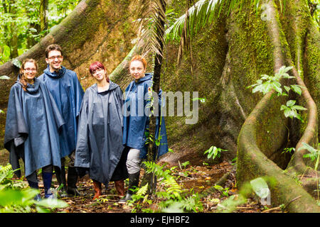 Gruppe von vier Touristen in Amazonas Dschungel gegen großen Ceiba-baum Regen Ponchos und Gummistiefel sind ein Muss in dieser Ecke der Natur Stockfoto