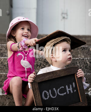 Freche Schwester trifft ihr Bruder über den Kopf mit Tafel Stockfoto