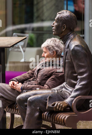 Frau sitzt auf der Bank neben Bronze Statue eines Mannes, New York City, USA Stockfoto