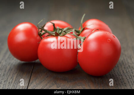 Reife nasse Tomaten an Rebstöcken auf Holztisch Stockfoto