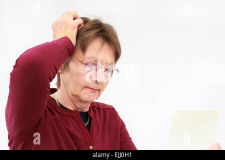 Ein besorgter älterer Frau Kratzer den Kopf beim Lesen ein verwirrendes schreiben Sie hält und Denken. England, Großbritannien, Großbritannien Stockfoto